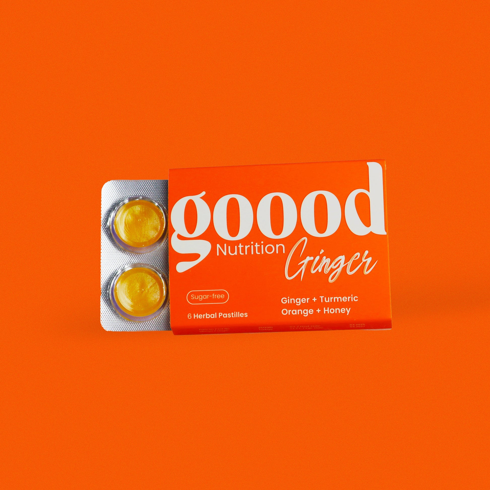 Opened Goood Nutrition Ginger box showing two golden herbal pastilles in blister pack, with a bright orange background.